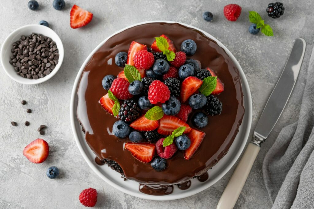 Delicious chocolate cake with chocolate glaze and fresh berries on a gray concrete background