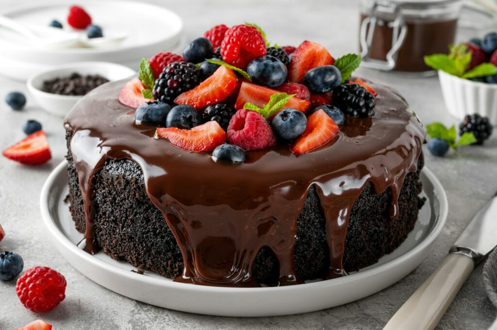 Delicious chocolate cake with chocolate glaze and fresh berries on a gray concrete background