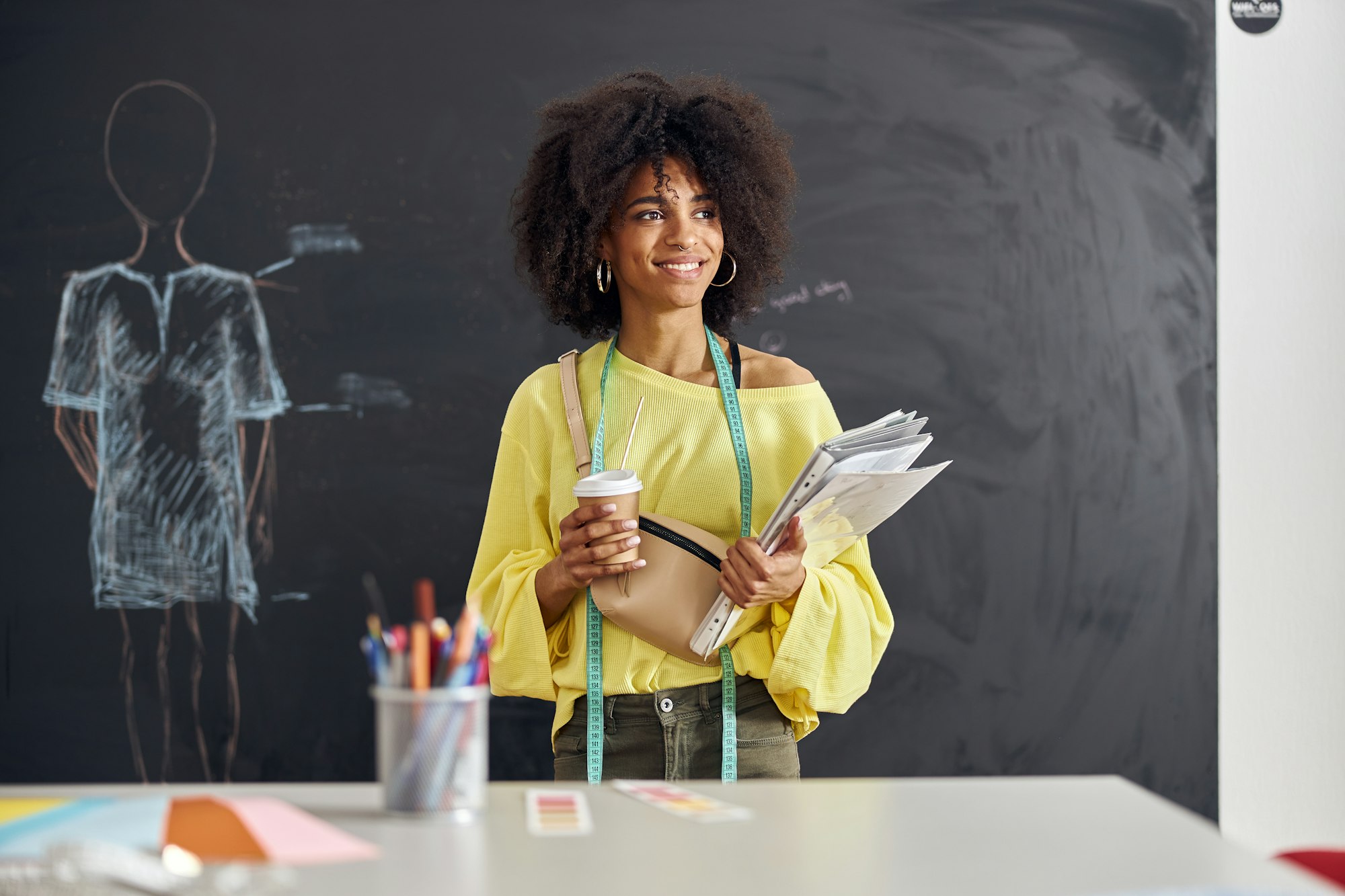 Smiling African-American teacher stands at table against blackboard with drawn human figure at